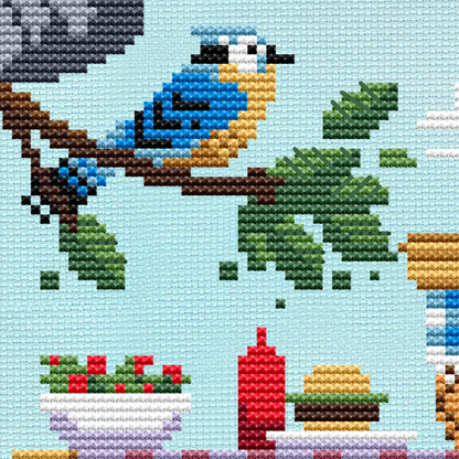 Cross stitch pattern of a blue jay sitting on a branch. BBQ food sits on the table